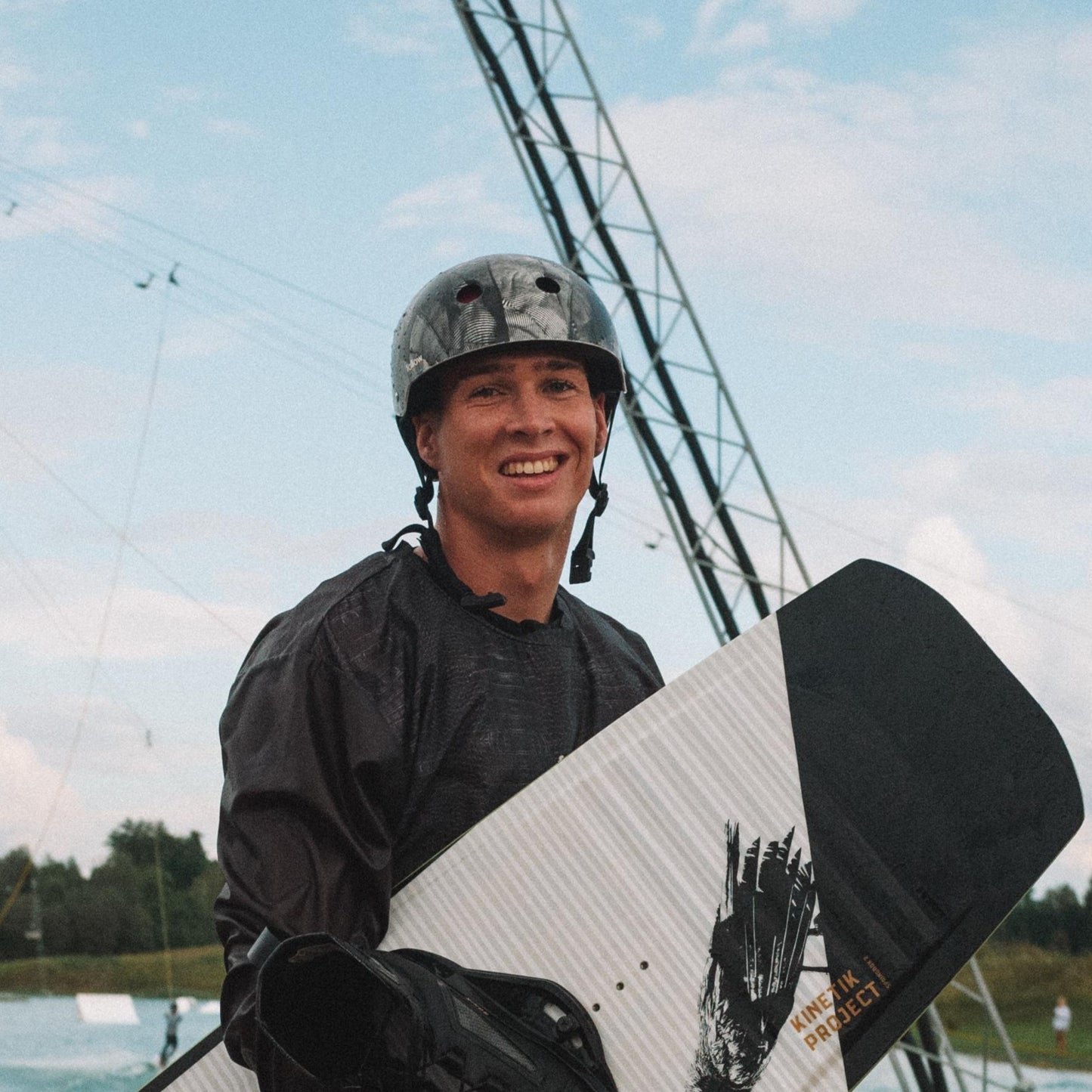 Wakeboarder mit Helm und Board lacht in Kamera