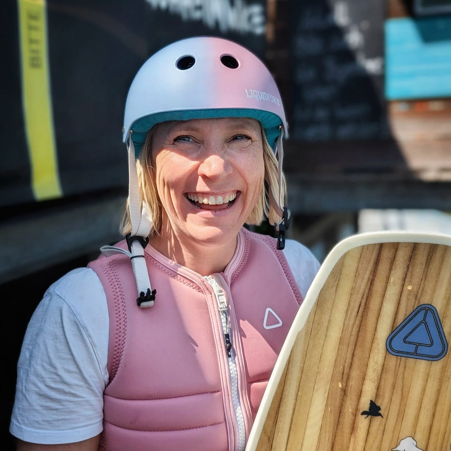 Wakeboarderin mit Helm und Board lacht in die Kamera